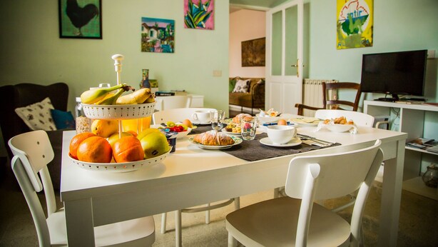 Un coin repas avec une table blanche dressée pour le petit-déjeuner, où l’on trouve des fruits, des viennoiseries et des boissons.