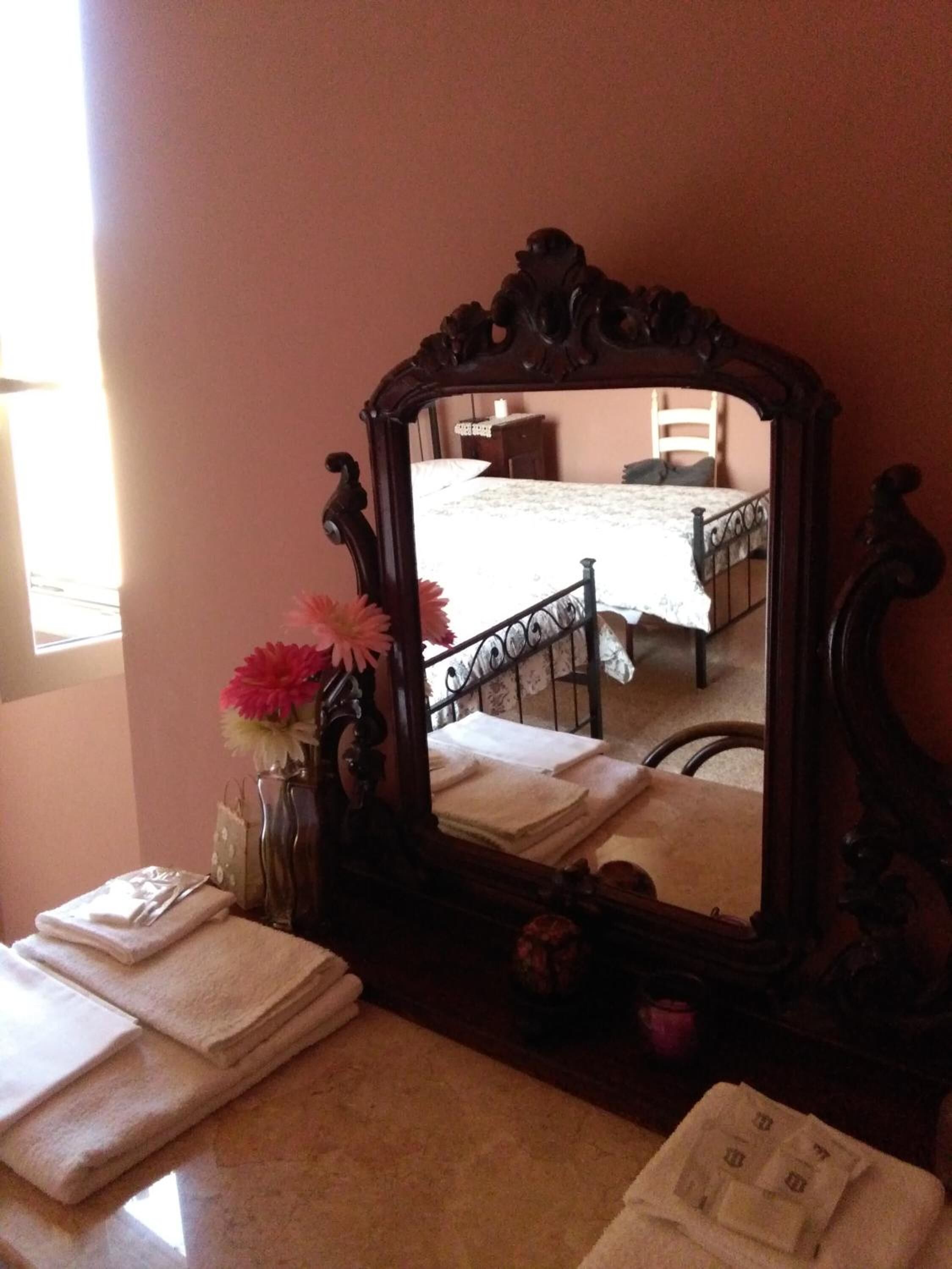 A mirror with a dark frame, a vase with pink flowers, and folded towels on a table.