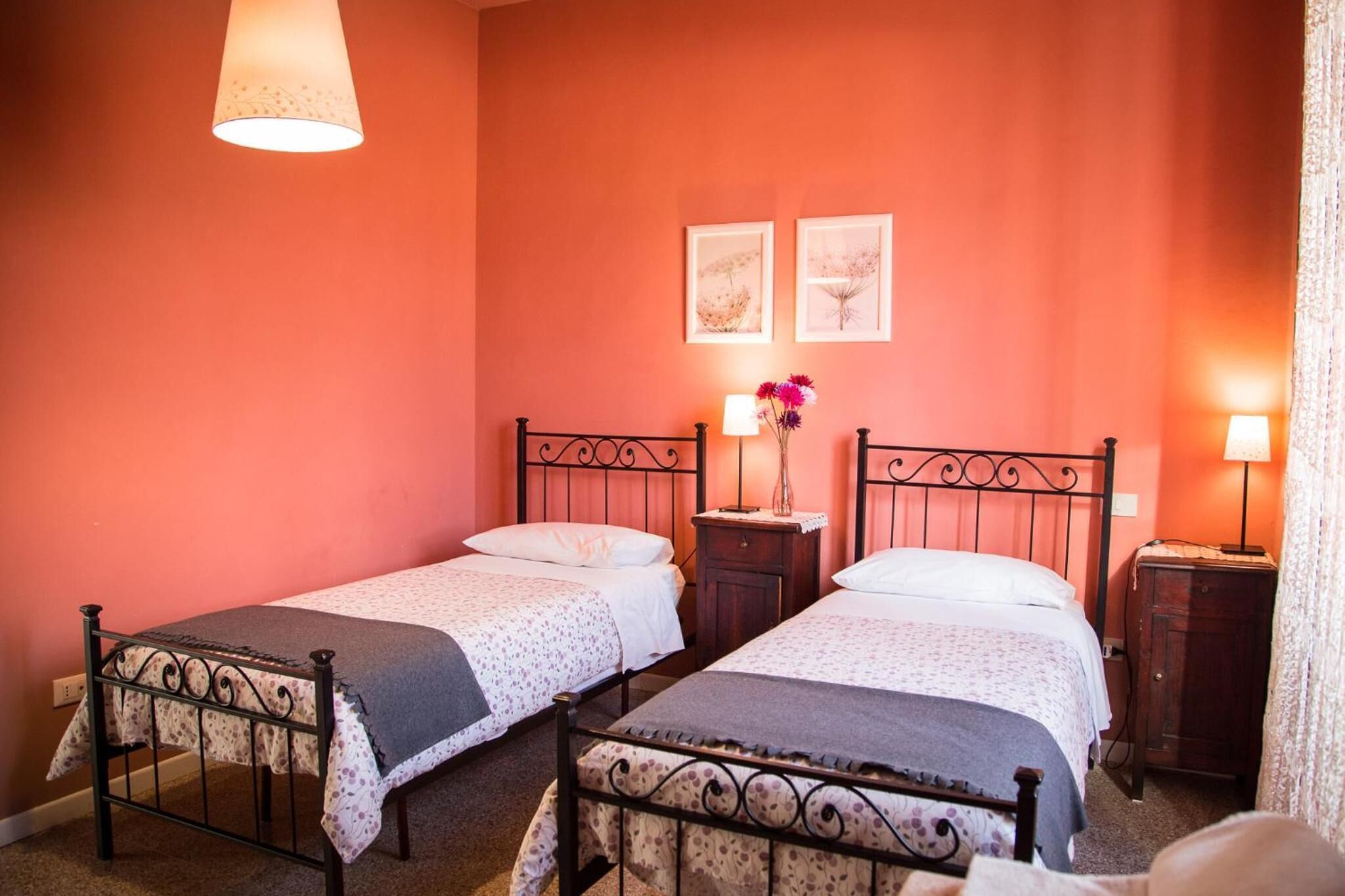 Ein Zimmer mit zwei Betten, jeweils mit Kopfteil, Nachttisch und Lampe. An der Wand hängen zwei Bilder in Rahmen.