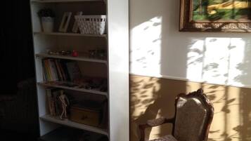 A room with a white bookshelf filled with books and decorative items, a wooden chair with a cushion, and a painting on the wall.