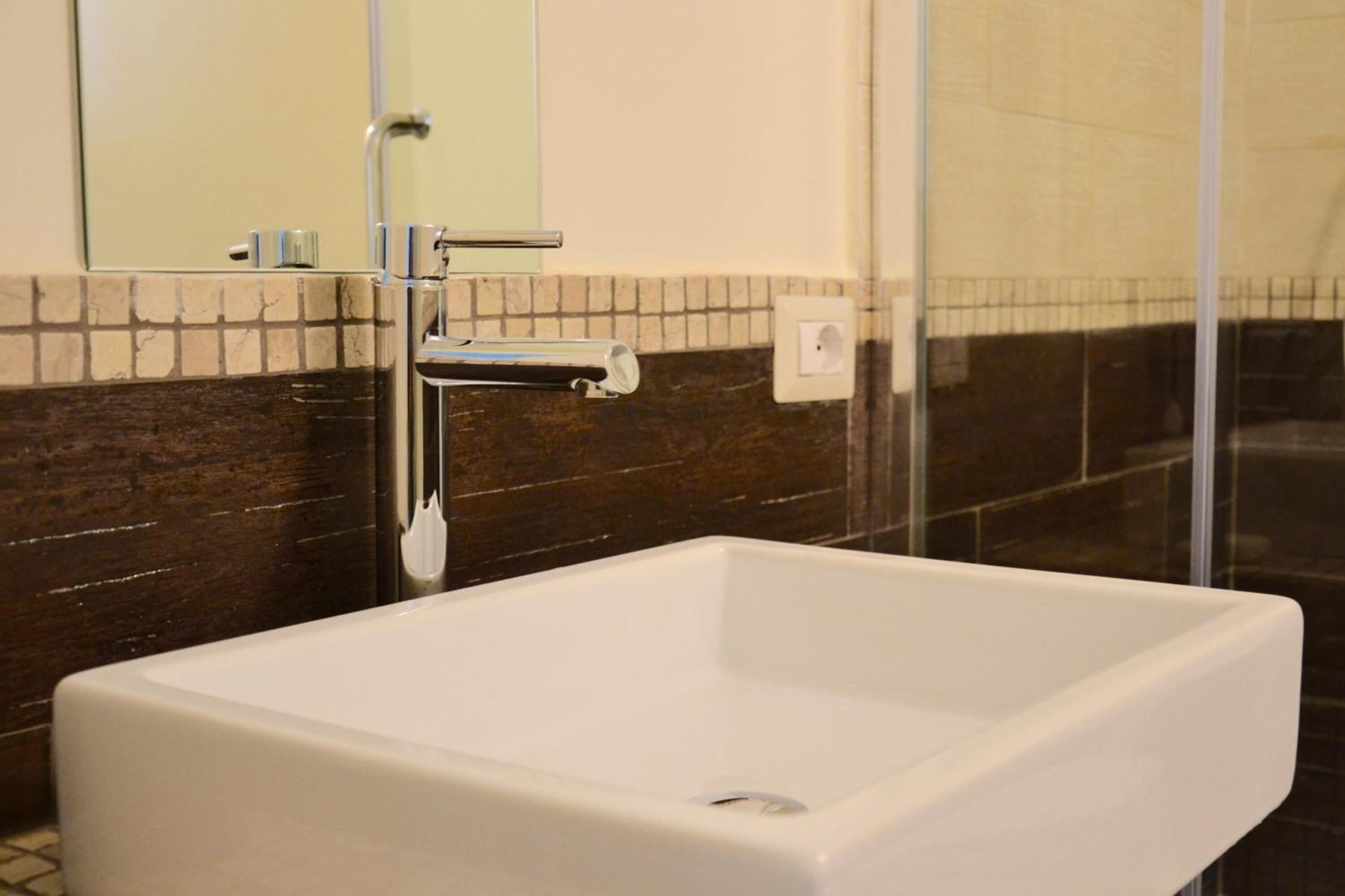 Une salle de bain moderne avec un lavabo blanc, une douche en verre et un mur recouvert de carreaux.
