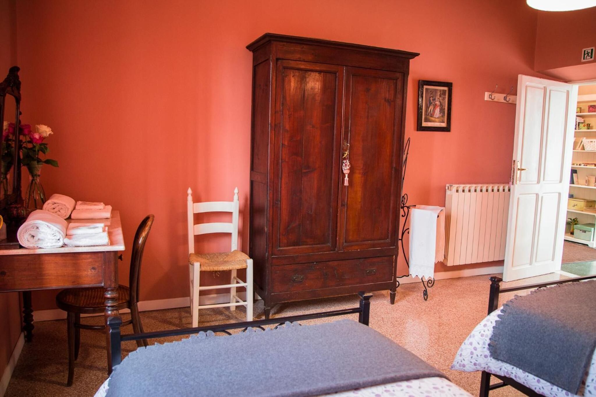 A room with a wooden cabinet, a chair, a table with towels, and a bed.