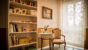 Une pièce comprenant une bibliothèque, une table agrémentée d’objets décoratifs, une chaise et une fenêtre ornée de rideaux en dentelle.