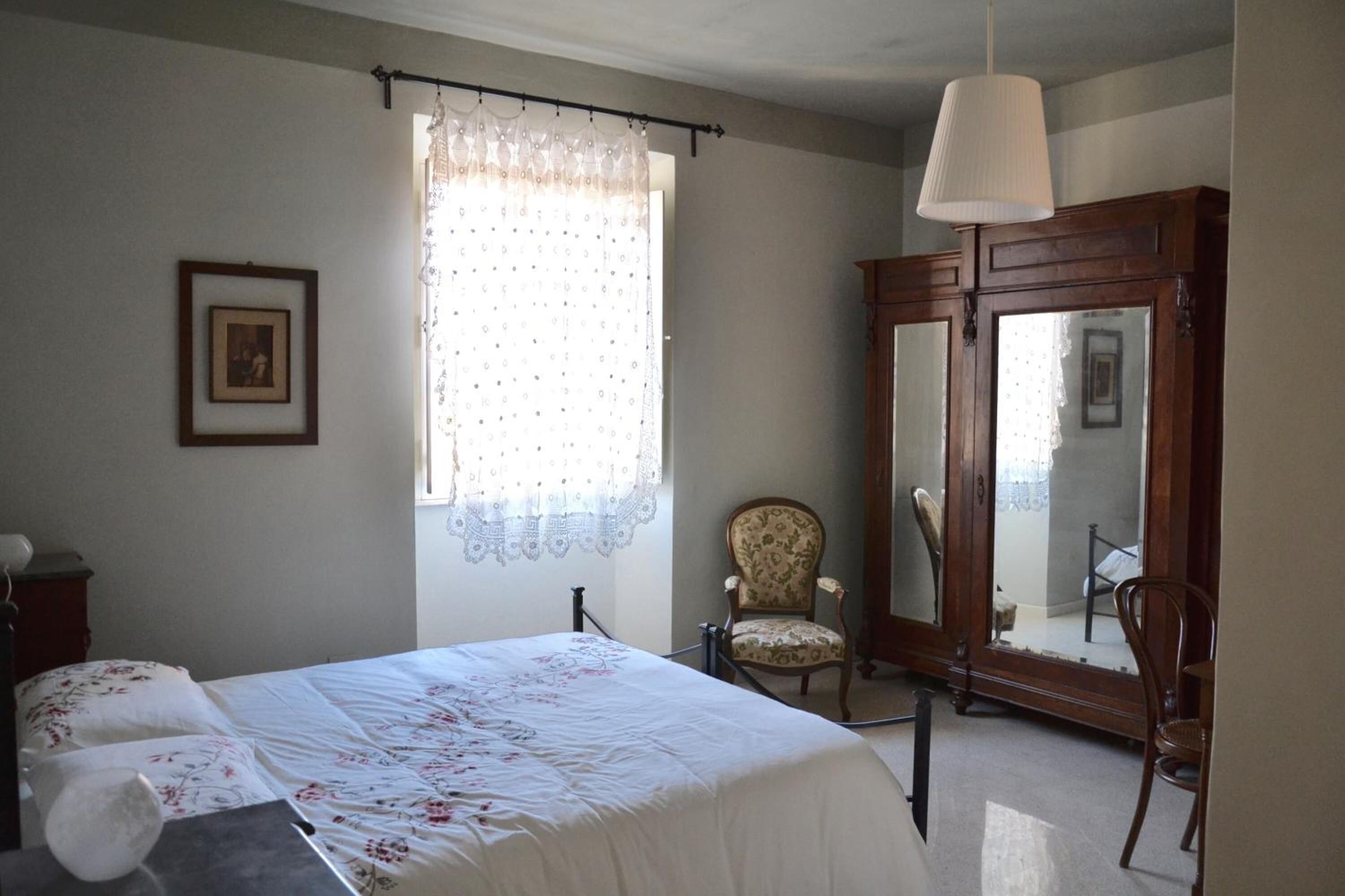 A bedroom with a bed, a chair, a wardrobe, and a window with curtains.