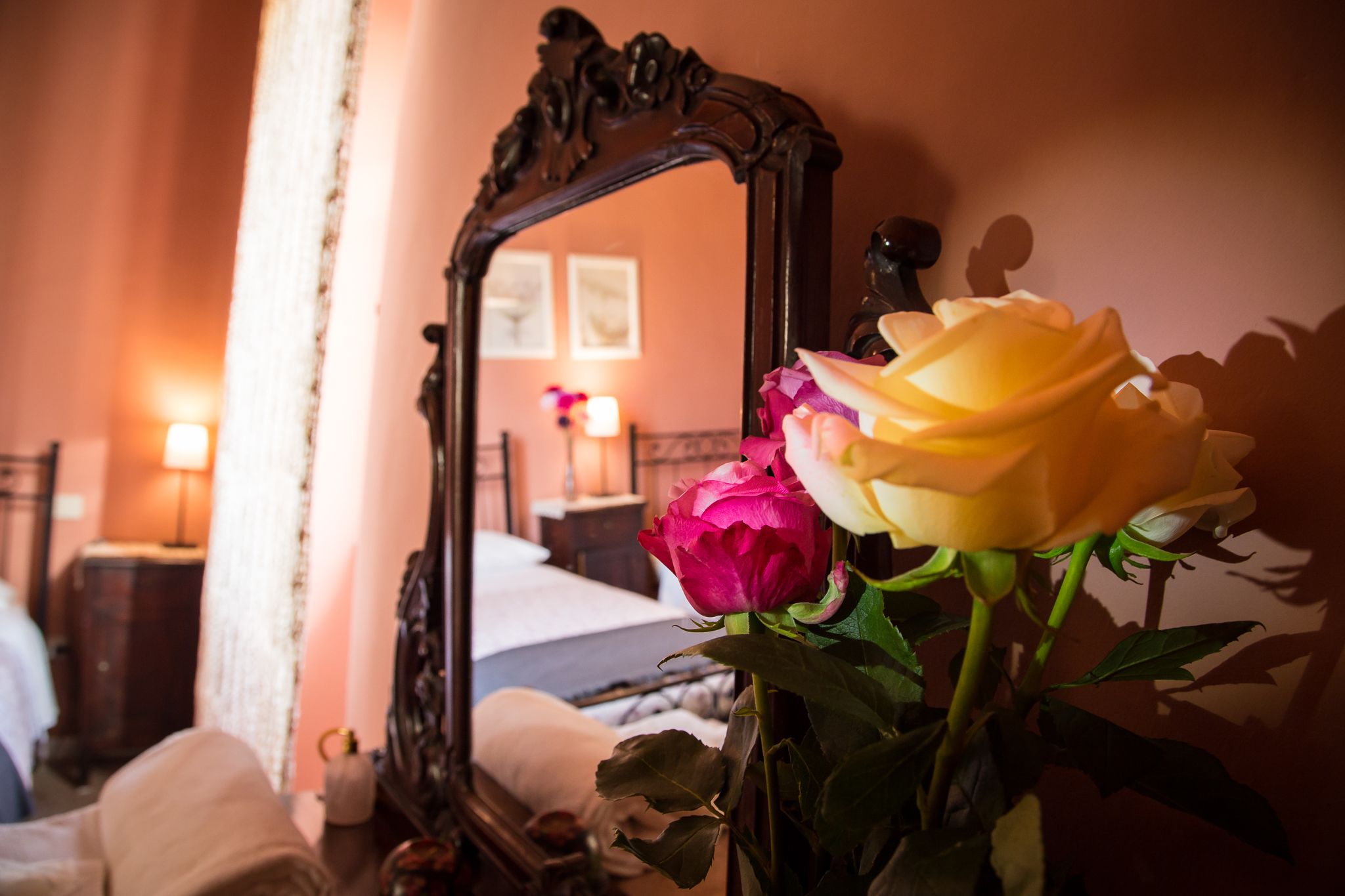 Un dormitorio con cama, mesita de noche, espejo y un jarrón con flores.