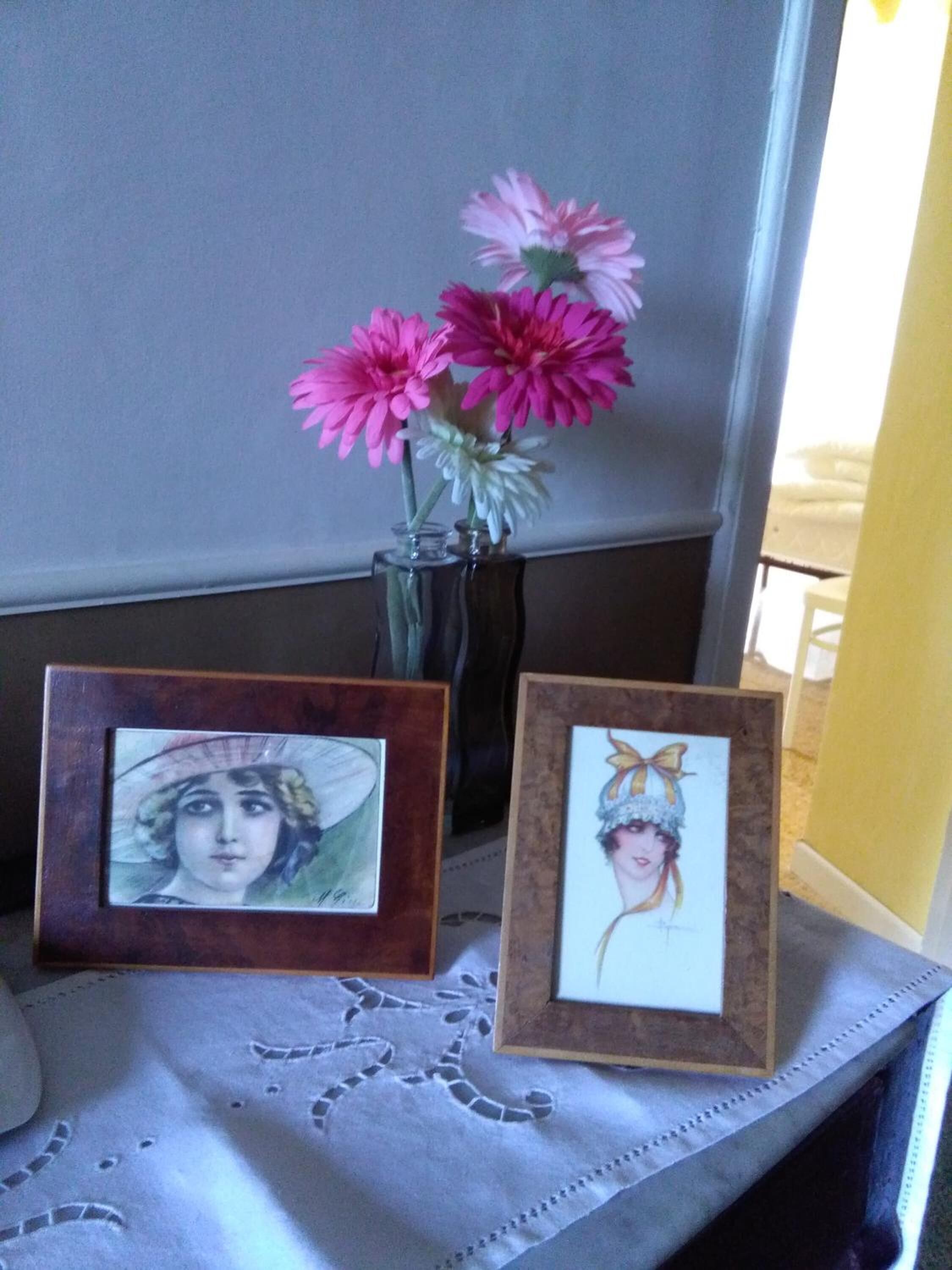 Una mesa con dos cuadros enmarcados y un jarrón de flores rosadas.