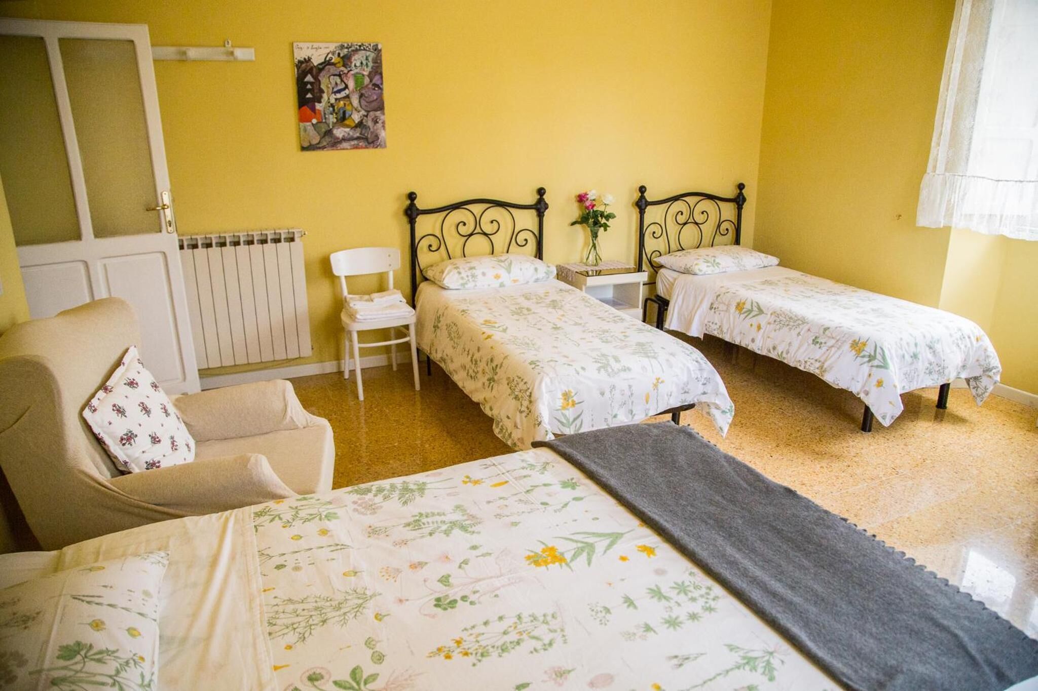 Una habitación con dos camas, una silla, un radiador y un cuadro en la pared.