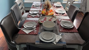 A dining room with a chandelier, a table set for four, and two windows with curtains.