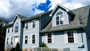 A two-story house with a gabled roof, multiple windows with shutters, and a front porch with steps.