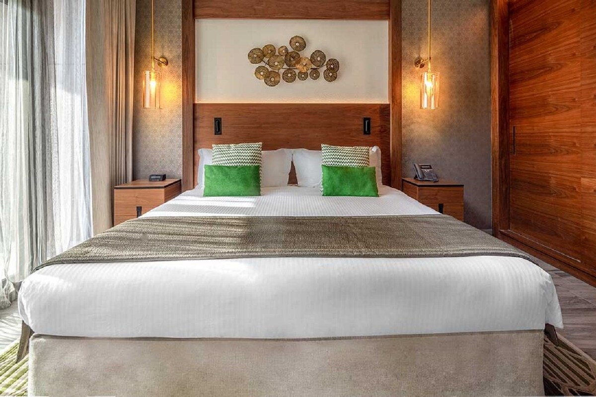 A hotel room with a large bed, two nightstands, a wall-mounted light fixture, and a decorative wall piece.