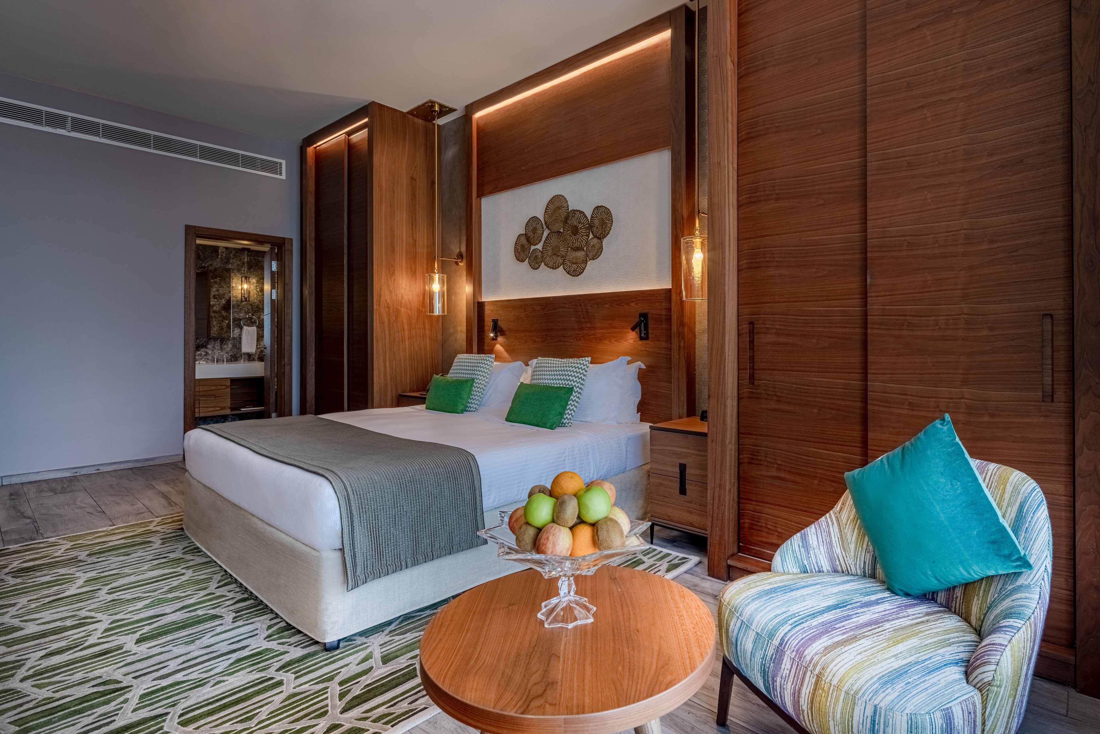 Un dormitorio moderno con una cama, una mesita de noche y una mesa redonda de madera con fruta.