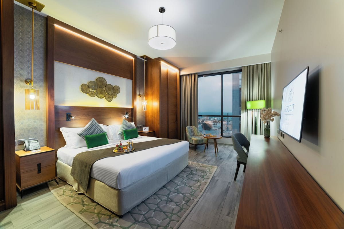 Habitación de hotel con una cama grande, un escritorio con una silla, un televisor y vistas a la ciudad.