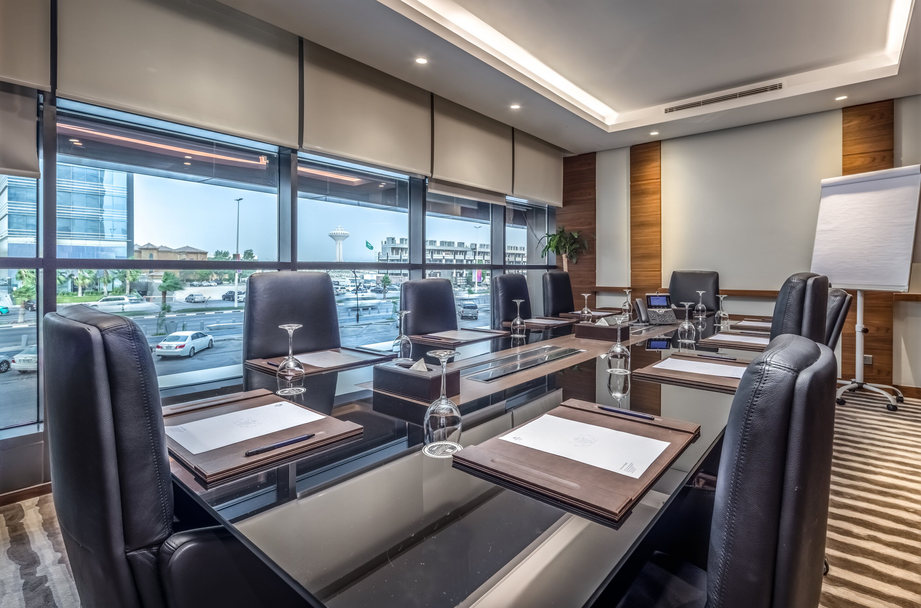 A modern conference room with large windows, leather chairs, a glass table, and a whiteboard.