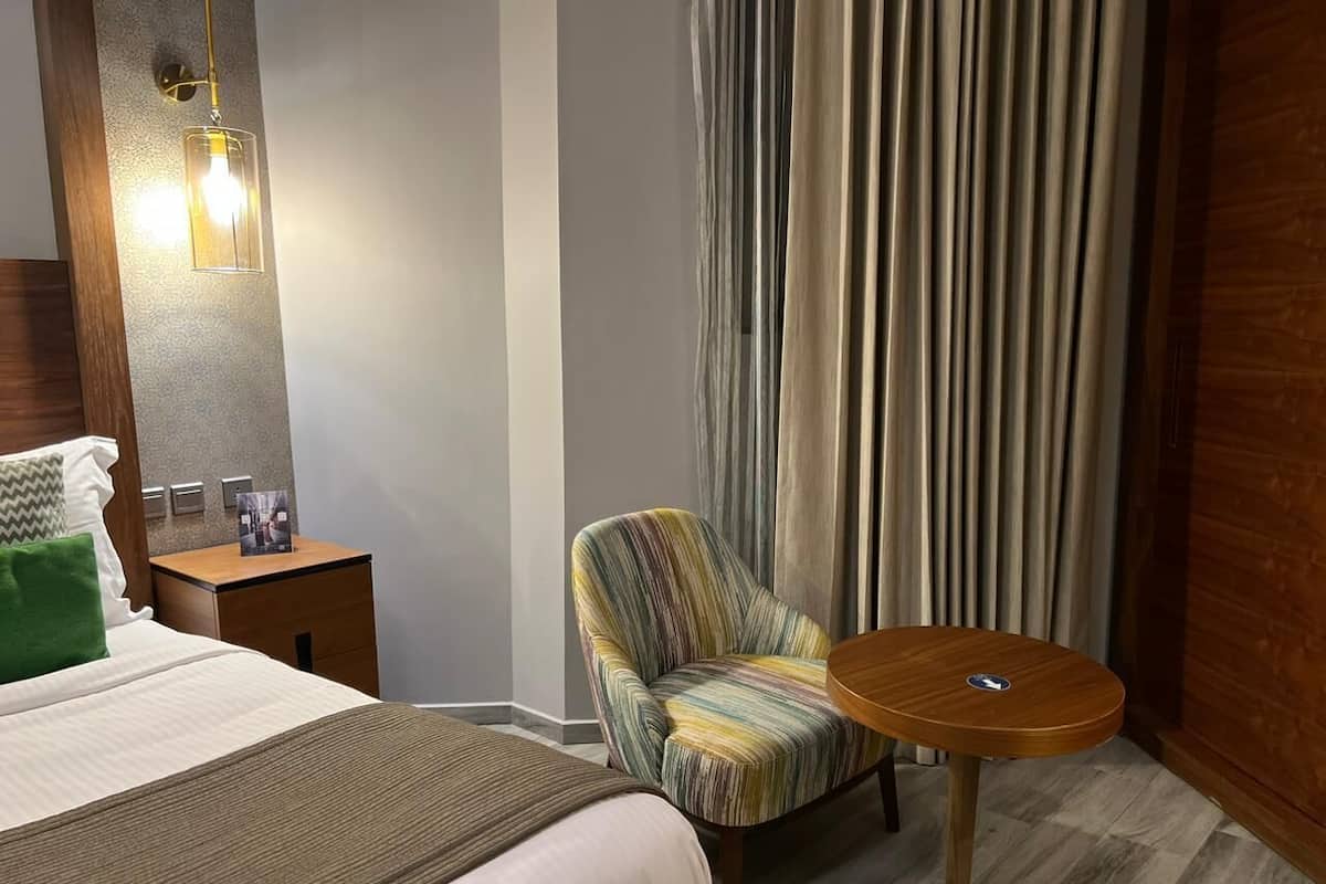 Una habitación de hotel con cama, mesita de noche, silla, mesa redonda y cortina.