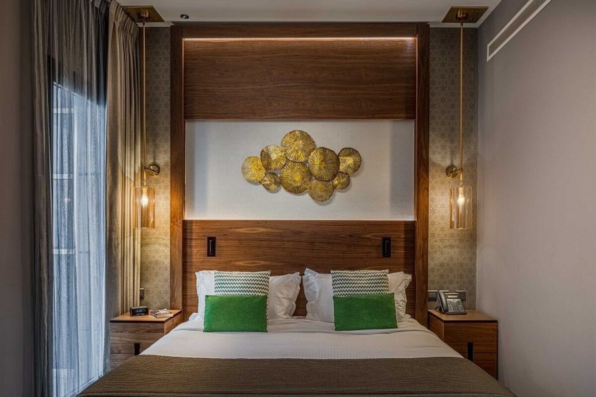 Una habitación de hotel con una cama grande, un banco, una lámpara de pared y un adorno mural.
