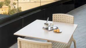 Varanda com mesa e cadeiras, vista para um horizonte costeiro com uma torre imponente e um porto de recreio.