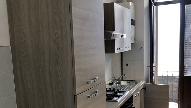 Une cuisine moderne avec des meubles en bois, un four encastré et une fenêtre équipée de stores.