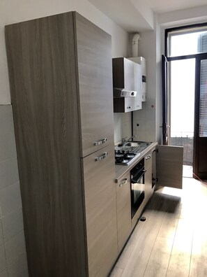 A modern kitchen with wooden cabinets, a built-in oven, and a window with blinds. - Sesto Apartment (Sesto San Giovanni)