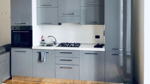Une cuisine moderne avec des meubles gris, un plan de travail blanc, un four encastré, une cuisinière à gaz et un réfrigérateur.