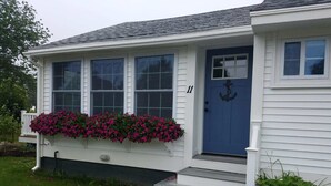 Una casa a un piano con una porta blu, rivestimento bianco e un piccolo portico con gradini.