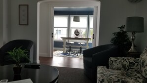 Un soggiorno con un divano nero, una poltrona a fantasia, un tavolino da caffè e una zona pranzo con tavolo e sedie.