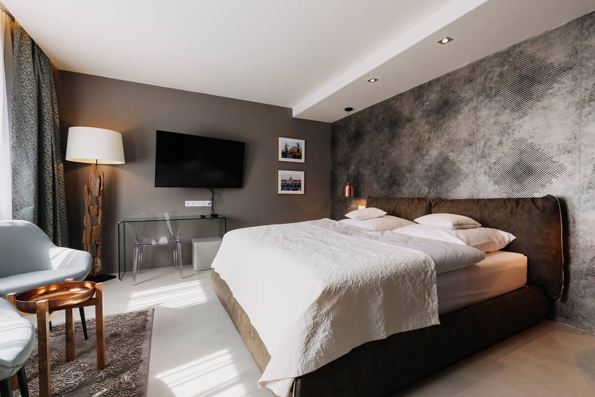 A modern bedroom with a large bed, a flat-screen TV, a glass desk, and a chair.