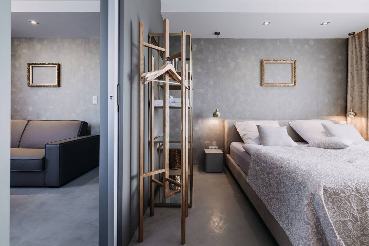 A modern bedroom with a bed, a sofa, a wooden hanger rack, and two framed pictures on the walls.
