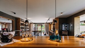 A modern bar area with a wooden counter, wine glasses, and a refrigerator. - VILLA BRICOLA - Boutique Apartments (Karlovy Vary)