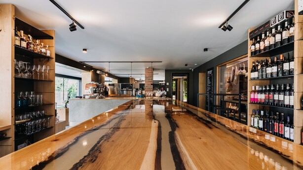 A modern bar area with wooden flooring, shelves of bottles, and glasses. - VILLA BRICOLA - Boutique Apartments (Karlovy Vary)