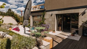 An outdoor patio area with a wooden deck, green metal chairs, a table, and a potted plant. - VILLA BRICOLA - Boutique Apartments (Karlovy Vary)
