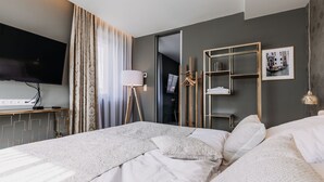 A modern hotel room with a large bed, a flat-screen TV, a desk with a lamp, and a wardrobe. - VILLA BRICOLA - Boutique Apartments (Karlovy Vary)