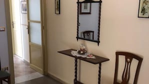 A hallway with a wooden chair, a small table with a decorative item, a mirror, and a framed picture on the wall. - Calatafimi House Casa Vacanze Palermo (Palermo)
