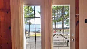 Une porte en bois avec un vitrage métallique en forme de grille, qui donne sur une terrasse extérieure équipée de tables de pique-nique et offrant une vue sur un lac.