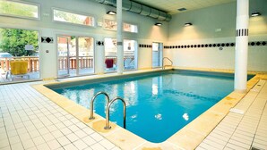Una piscina interior con paredes de vidrio transparente, suelo de baldosas y una escalera de natación.
