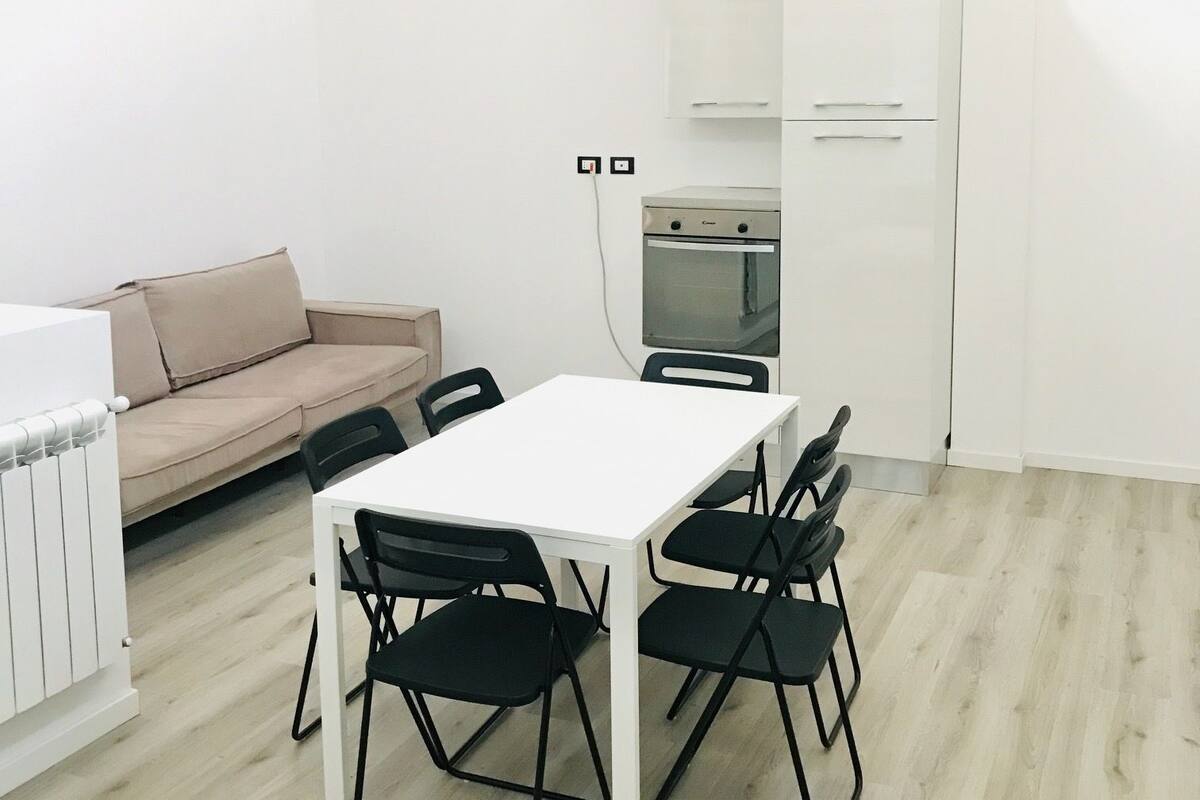 A modern, minimalistic living space with a white table and chairs, a beige sofa, and a built-in oven.