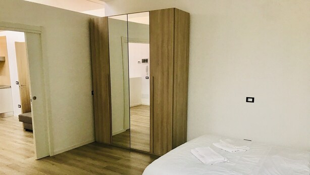 A bedroom with a large mirror, a wooden wardrobe, and a bed with white bedding. - Humanitas (Milan)