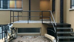 A building with a stone-paved courtyard, a bicycle, and a staircase leading to an upper level. - Humanitas (Milan)