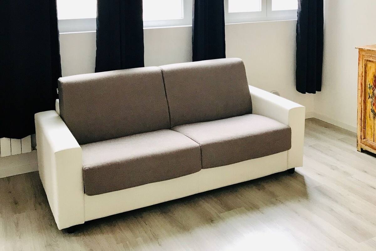 A modern living room with a beige sofa, large windows with black curtains, and a wooden cabinet.
