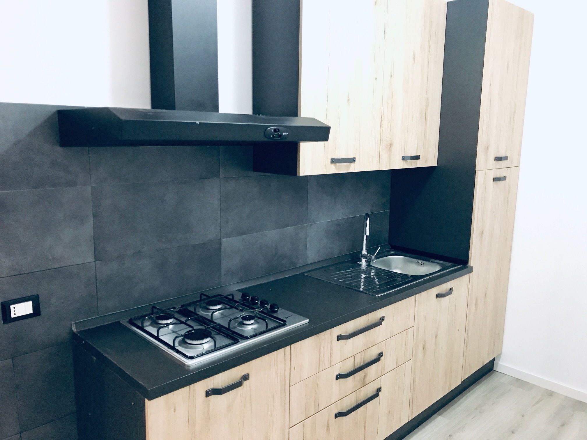 A modern kitchen with a gas stove, black countertop, wooden cabinets, and a black range hood.