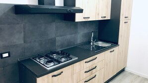 A modern kitchen with a gas stove, black countertop, wooden cabinets, and a black range hood. - Humanitas (Milan)