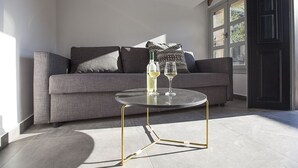 Una sala moderna con un sofá gris, una mesa redonda de vidrio con patas doradas y dos copas de vino sobre la mesa.