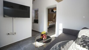 Una habitación de hotel moderna con un televisor de pantalla plana, una pequeña mesa con fruta, un sofá y un arco de piedra que da a un baño.