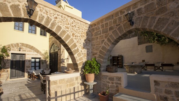 Un patio exterior con arcos de piedra, plantas en macetas y mobiliario para exteriores.
