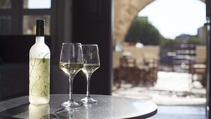 Una botella de vino blanco y dos copas sobre una mesa con vista a un patio al aire libre.