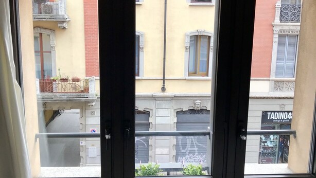 Uitzicht vanaf een balkon met drie ramen, op een straat met gebouwen en een winkel genaamd 