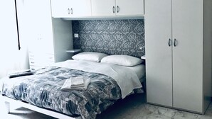 Een slaapkamer met een bed, een witte kledingkast, een hoofdbord met patroon en een nachtkastje.