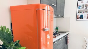 Een keuken met een fel oranje koelkast, een potplant en een betegelde vloer.