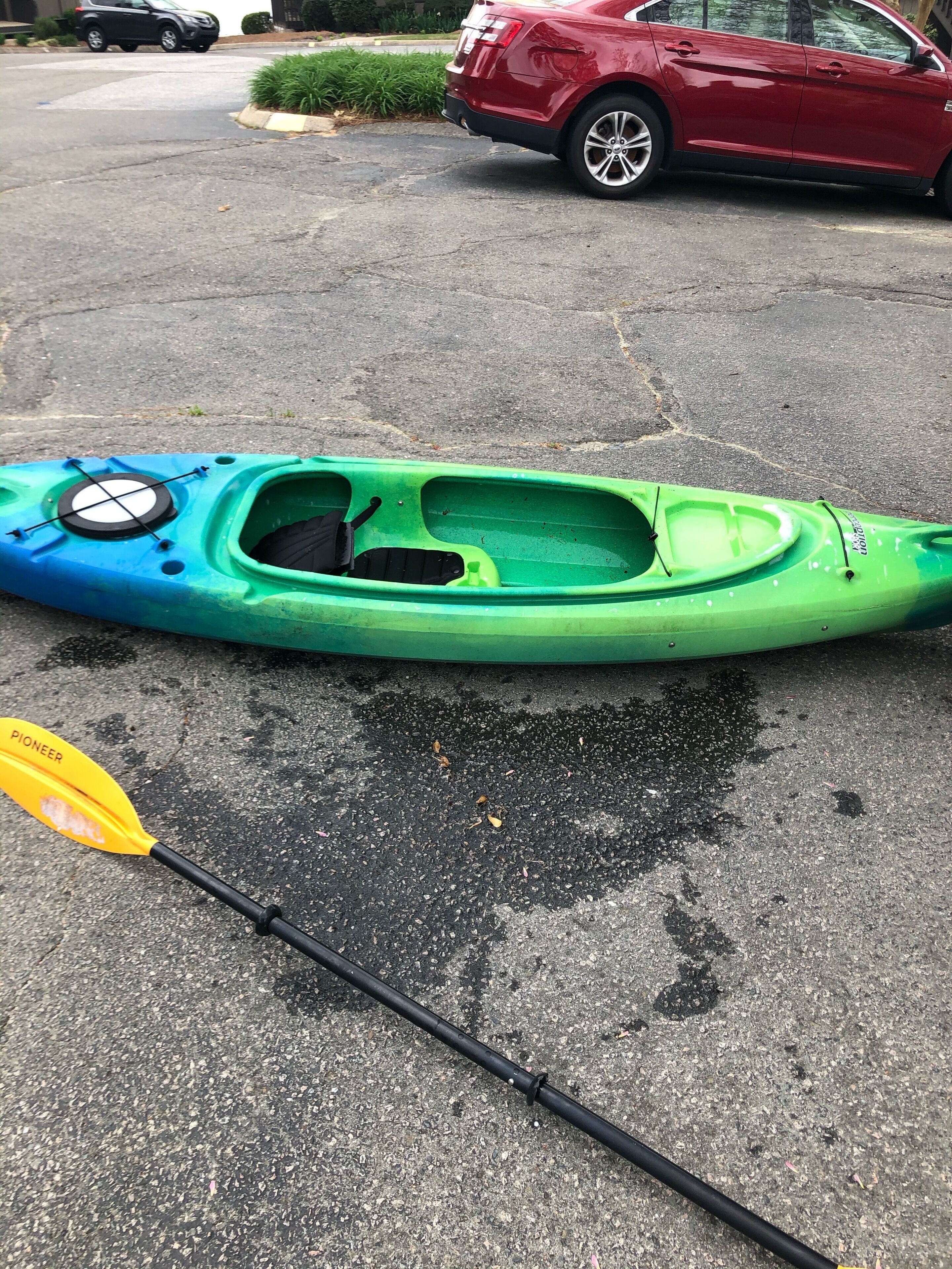 A green and blue kayak with a paddle on a paved surface.