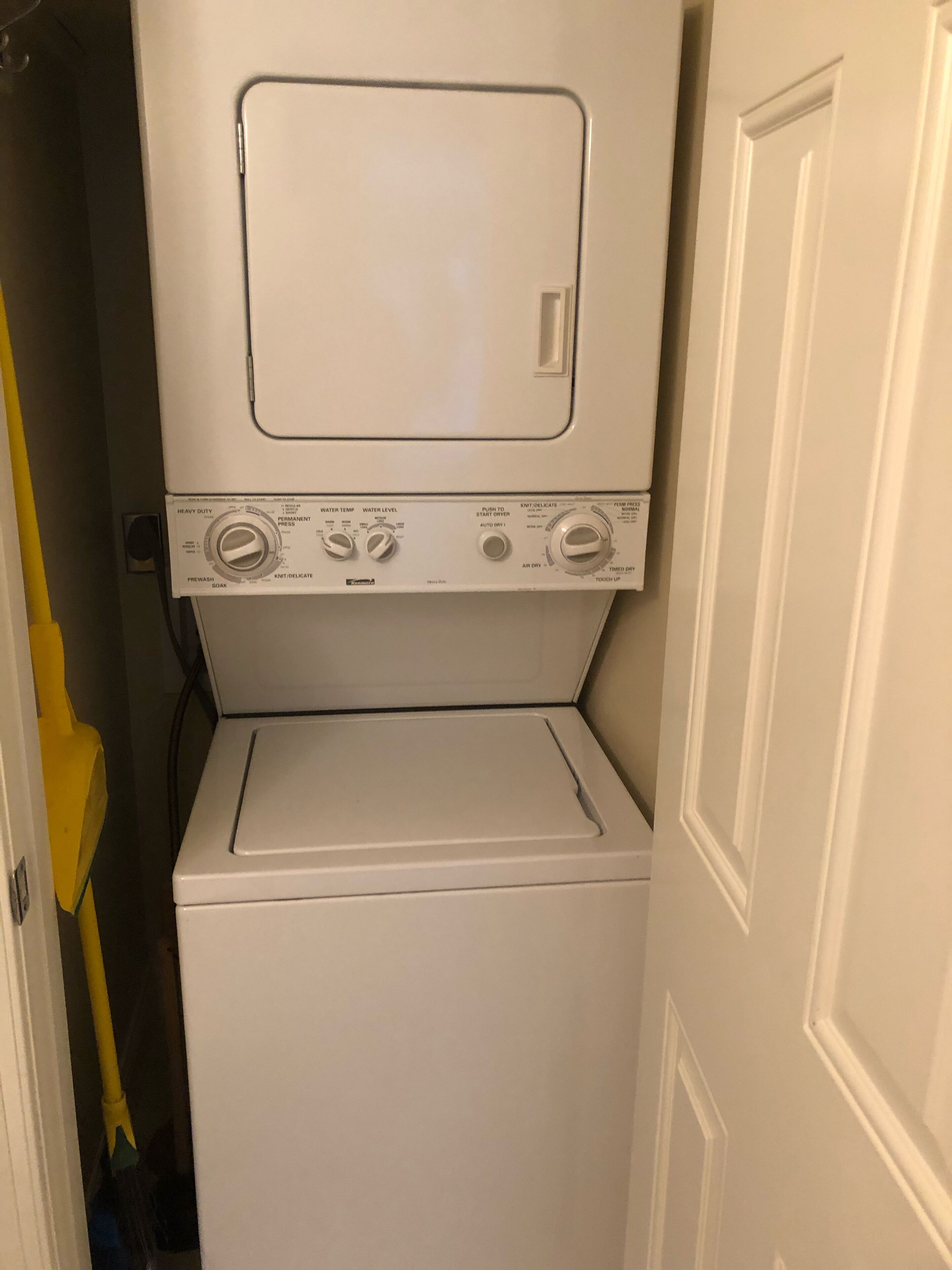 A compact, white, stacked washer and dryer unit in a narrow hallway.