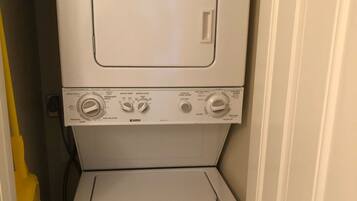 A compact, white, stacked washer and dryer unit in a narrow hallway.